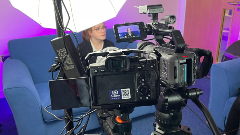 A young woman is sitting on a sofa being filmed.