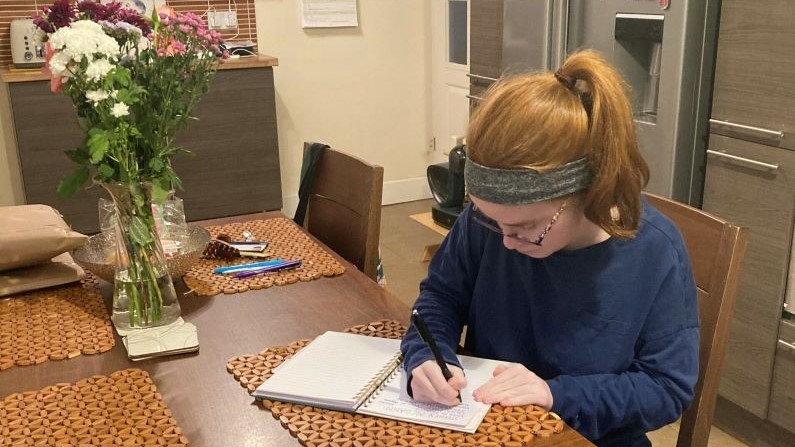 Lucy sitting at a kitchen table writing.